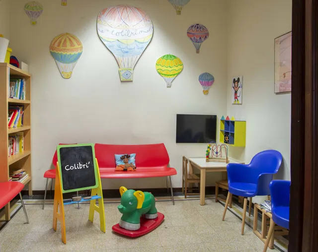 La sala d’attesa dello studio, con mongolfiere dipinte sulle pareti, un divano rosso e una lavagnetta con la scritta Colibrì
