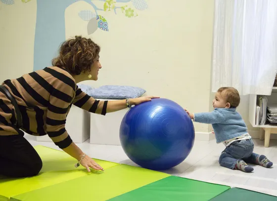 La psicomotricista Sara Solinas gioca con un bambino piccolo appoggiato a una grande palla